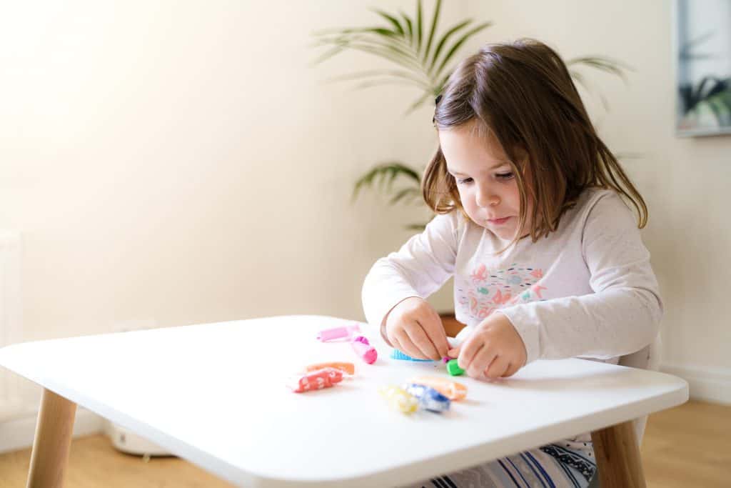 Toddler girl playing plasticine dough in preschool homeschool. Creative education, motor skills development. Homeschool concept. 